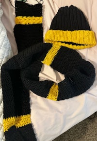 a black and yellow knitted scarf and hat on a bed