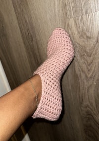 a woman wearing pink crocheted slippers on a wooden floor