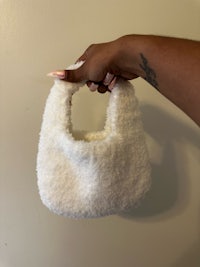 a hand holding a white fuzzy bag