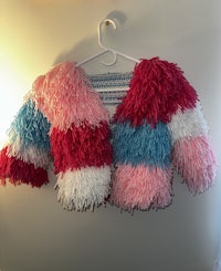 a pink, blue, and white sweater hanging on a hanger